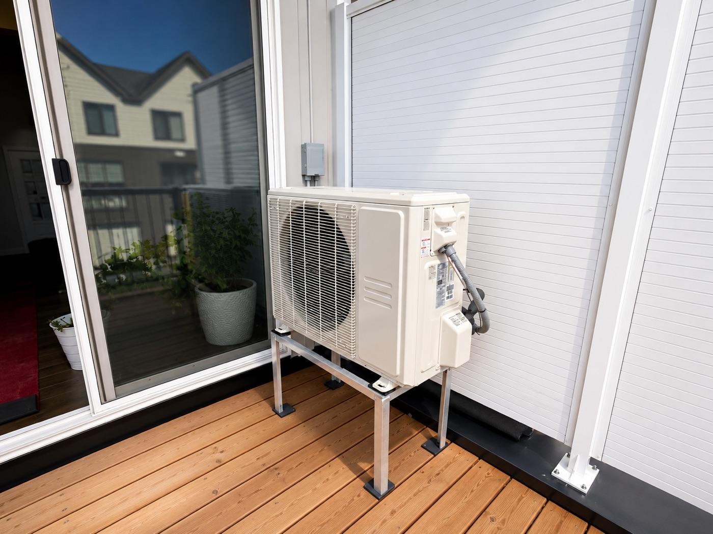 Heat pump outdoor unit mounted on a raised bracket beside a home